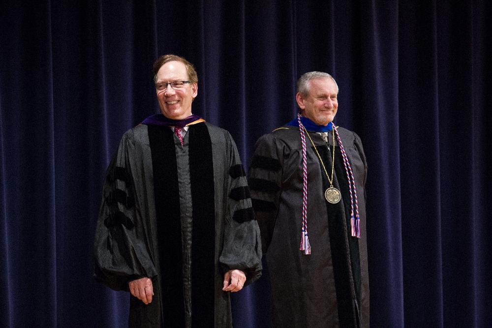 Two faculty members smile on stage